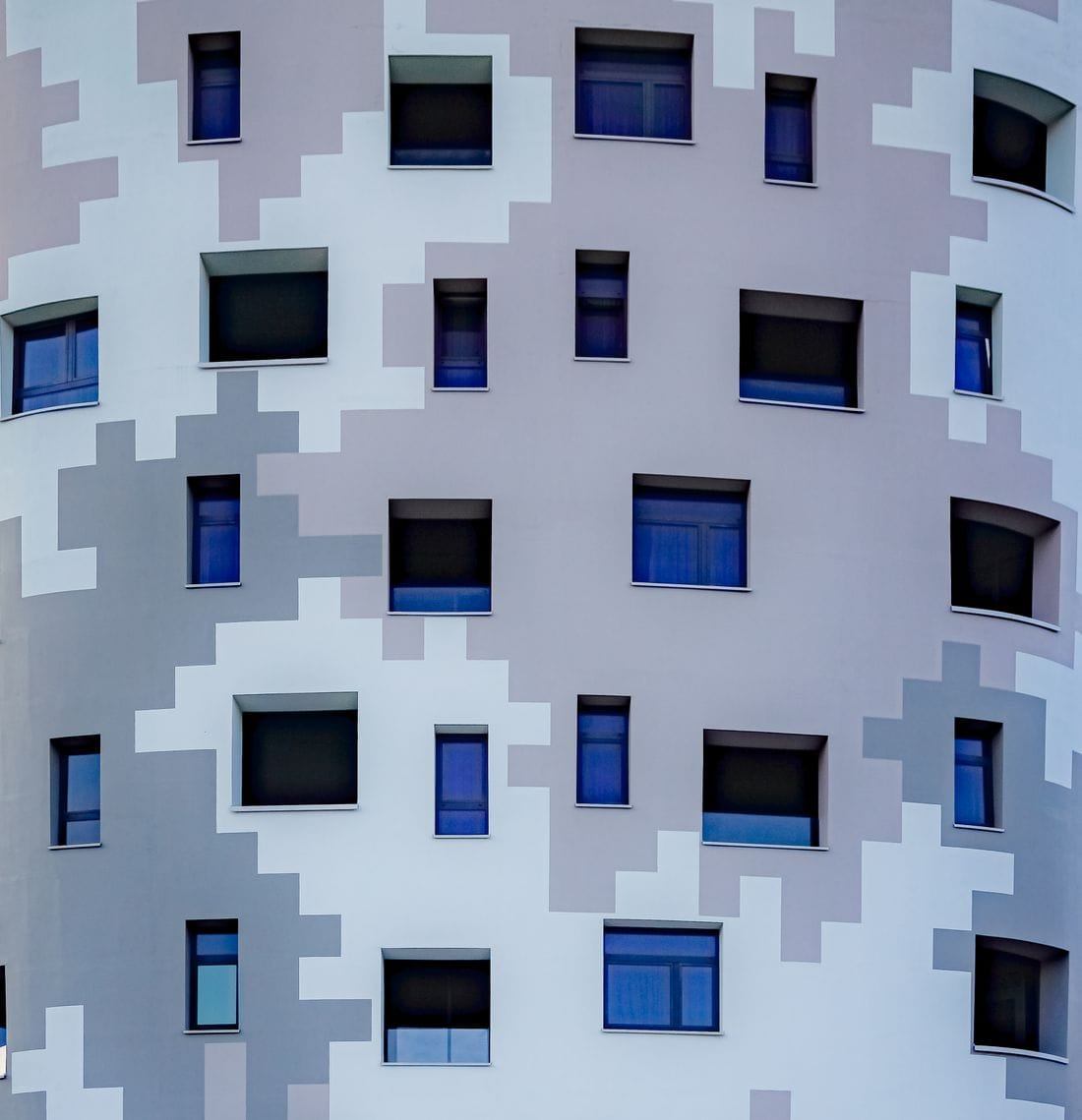 Fachada de um edifício com dezenas de janelas quase iguais, em cinza e azul.