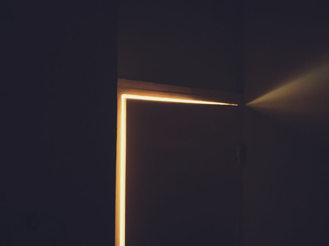 Uma fresta de luz escapando pela lateral de uma porta fechada, num quarto escuro.